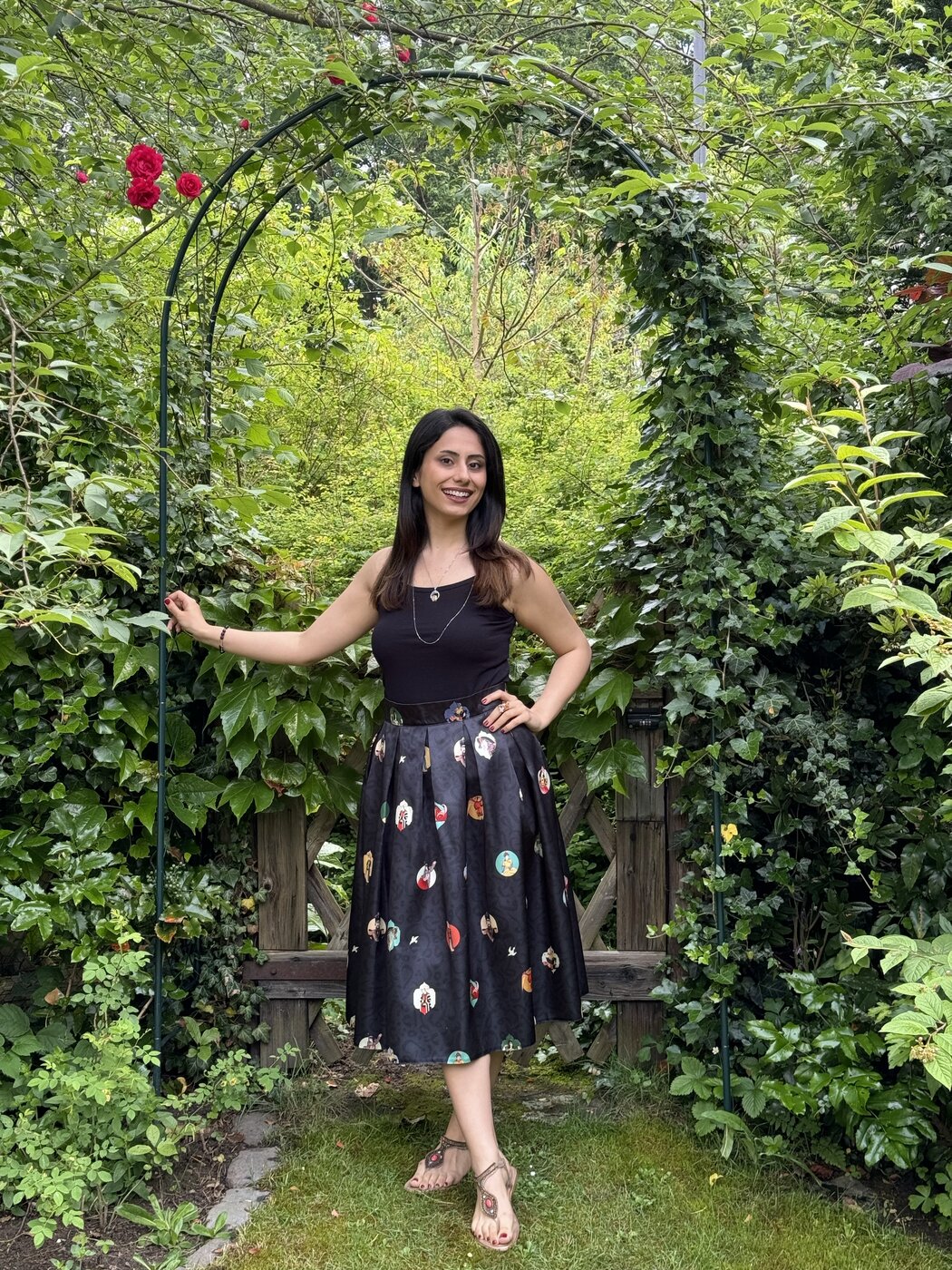 Mina standing under a rose arch in a green garden
